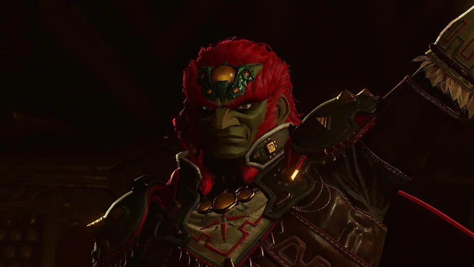 Close-up of Ganondorf's face in the dark: red hair, green skin, amber eyes, a green-and-gold jewelled piece on his forehead, dark armor with red Gerudo patterning and a gold chest ornament